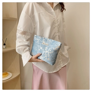 Detail of light blue floral makeup bag with pleated texture held by a model