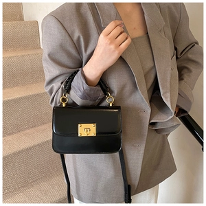 Détail du sac bandoulière noir avec boucle à rivet doré et poignée tissée sur blazer