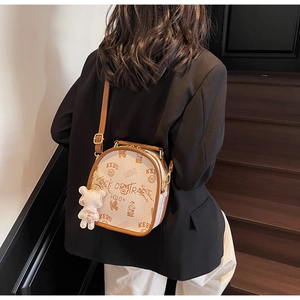 Chic cream graffiti crossbody bag with brown leather trim shown in a lifestyle setting