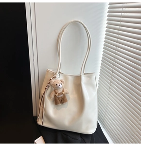 Detail view of cream leather tote bag with a cute plush bear pendant and thin straps