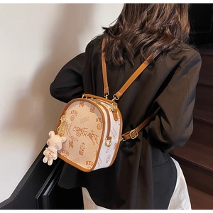 Detail of a beige graffiti backpack with plush bear charm worn on a black blazer