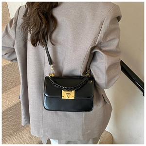 Détail du sac bandoulière noir brillant avec poignée tressée et fermoir doré sur un mannequin