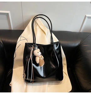 Detail of glossy black tote bag on leather sofa with a cute bear plush charm accessory