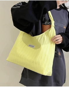 Detail of the bright yellow pleated nylon tote bag featuring a white woven brand label