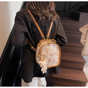 Detail view of stylish white backpack with brown leather trim and cute bear charm