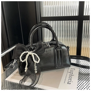 Détail du sac Boston noir en cuir verni brillant avec breloque ruban et perle décorative