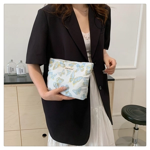 Detail of a white canvas zipper pouch with blue butterfly prints held by a model