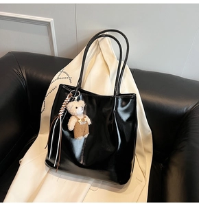 Detail of glossy black tote bag with cute teddy bear charm on a minimalist background