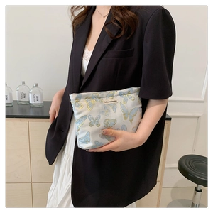 Woman holding a white woven cosmetic bag featuring blue butterfly prints in a lifestyle setting
