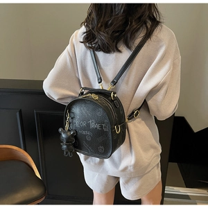 Rear view of a black pebbled leather mini backpack with graffiti print and a bear charm