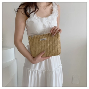 Detail of woven straw makeup bag with brand label held by a model in a lace dress