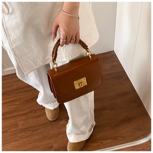 Détail d'un sac bandoulière marron avec poignée en cuir tressé et fermoir en métal doré
