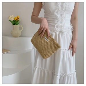 Detail of woven khaki makeup pouch with logo tag held by model in lace dress