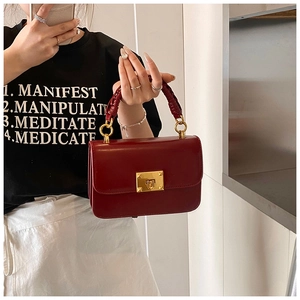 Détail du sac en cuir bordeaux avec poignée tressée et fermoir carré doré élégant