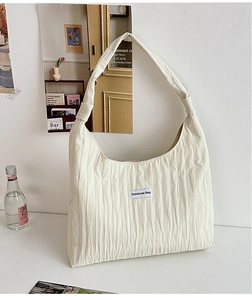 Detail of off-white pleated fabric tote bag featuring a stitched brand logo label