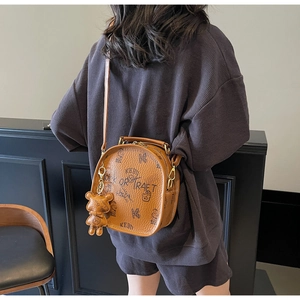 Detail of caramel leather backpack with graffiti print and a cute bear charm pendant