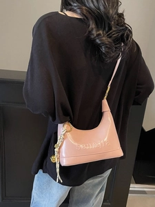 Pink patent leather dumpling bag with embossed logo and tassel detail shown on shoulder