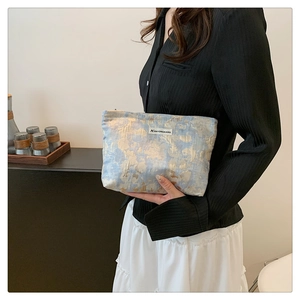 Detail of a vintage floral jacquard makeup bag with brand label held by a model