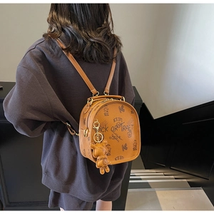 Macro view of brown PU leather backpack with graffiti prints and bear charm accessory