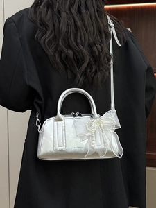 Sac Boston argenté avec nœud en tulle et perles porté sur un blazer noir chic