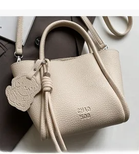 Vue détaillée du sac à main en cuir crème avec texture grainée et breloque ours