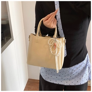 Detail of beige bucket bag featuring a faux pearl bow pendant and smooth leather texture