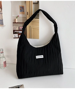 Close-up of black pleated tote bag fabric texture and white brand label on the front side