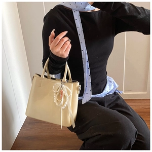 Detail of cream bucket bag with elegant pearl bow charm and smooth leather texture
