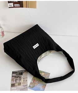 Detail showing pleated black tote bag texture and a white minimalist fabric brand label