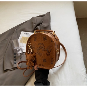 Brown retro leather handbag with vintage graphics and a cute bear charm on a grey blazer