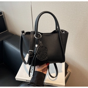 Détail du sac à main en cuir grainé noir avec logo embossé et breloque petit ours
