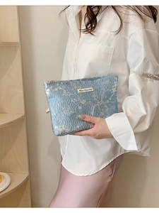 Blue textured fabric makeup bag with white floral pattern and brand label held by hand