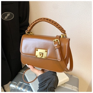 Détail d'un sac porté épaule en cuir caramel avec poignée tressée et boucle dorée carrée