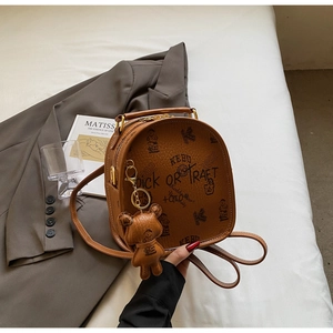 Detail of brown leather backpack with bear print and cute hanging charm on a bed
