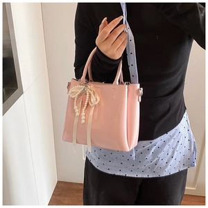 Detailed view of pink bucket bag featuring cream ribbon bow and pearl charm accessories