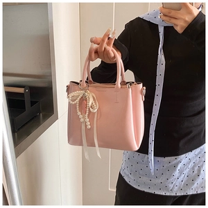 Detail of pink leather bucket bag featuring a white pearl and ribbon bow charm accessory