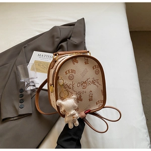 Detail of a beige PU leather mini backpack featuring bear prints and a matching charm