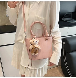 Borsa a secchiello rosa con trama litchi e ciondolo a forma di orsetto su modella