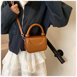 Brown mini square bag with thick curved handle and detachable shoulder strap on model