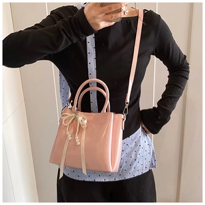 Pink bucket bag with glossy finish featuring white bow and elegant pearl charm detail