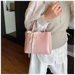 Detail of pink glossy bucket bag featuring pearl bow charm and white ribbon accent