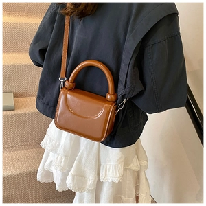 Caramel brown small square bag with round top handle shown as crossbody on model