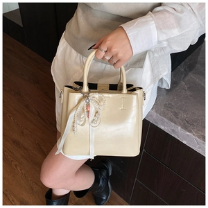 Detail of cream bucket bag featuring elegant pearl and white ribbon bow charm accessory