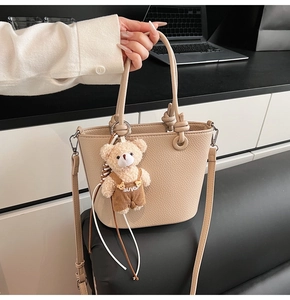 Dettaglio della borsa a secchiello beige con trama litchi e pendente a forma di orsetto