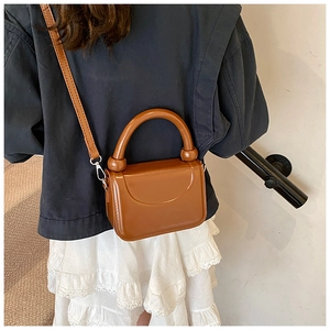 Detail of a brown glossy leather mini bag with thick round handle and metal strap buckle