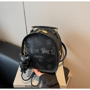 Detail of black pebbled leather backpack with graffiti prints and bear charm