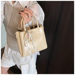 Detail of cream leather bucket bag with pearl charm and elegant ribbon handle decoration