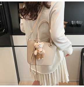 Dettaglio borsa a secchiello beige con trama a licchi e ciondolo a forma di orsetto