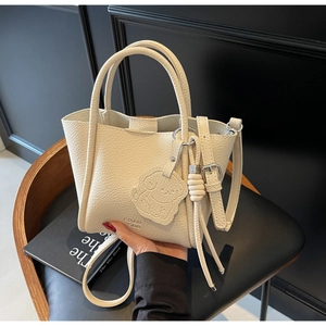 Détail d'un sac cabas en cuir crème avec breloque chien sur une chaise sombre