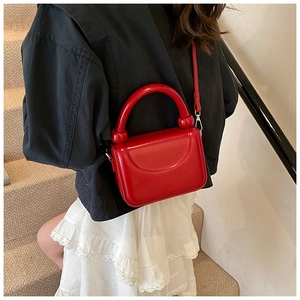 Close-up of a red leather mini square bag with a bold curved handle and thin shoulder strap
